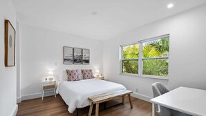 A bedroom with a bed, bedside tables, a desk, and a window with a view of greenery. - Sailors Rest Sailboat Bend (Fort Lauderdale)