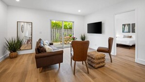 A modern living room with a sofa, chairs, a TV, and a large window. - Sailors Rest Sailboat Bend (Fort Lauderdale)