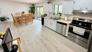 Una cocina moderna con comedor, que incluye electrodomésticos de acero inoxidable, armarios blancos y una mesa de comedor de madera.