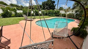 Un patio trasero con piscina, dos sillas hamaca y una planta en maceta.