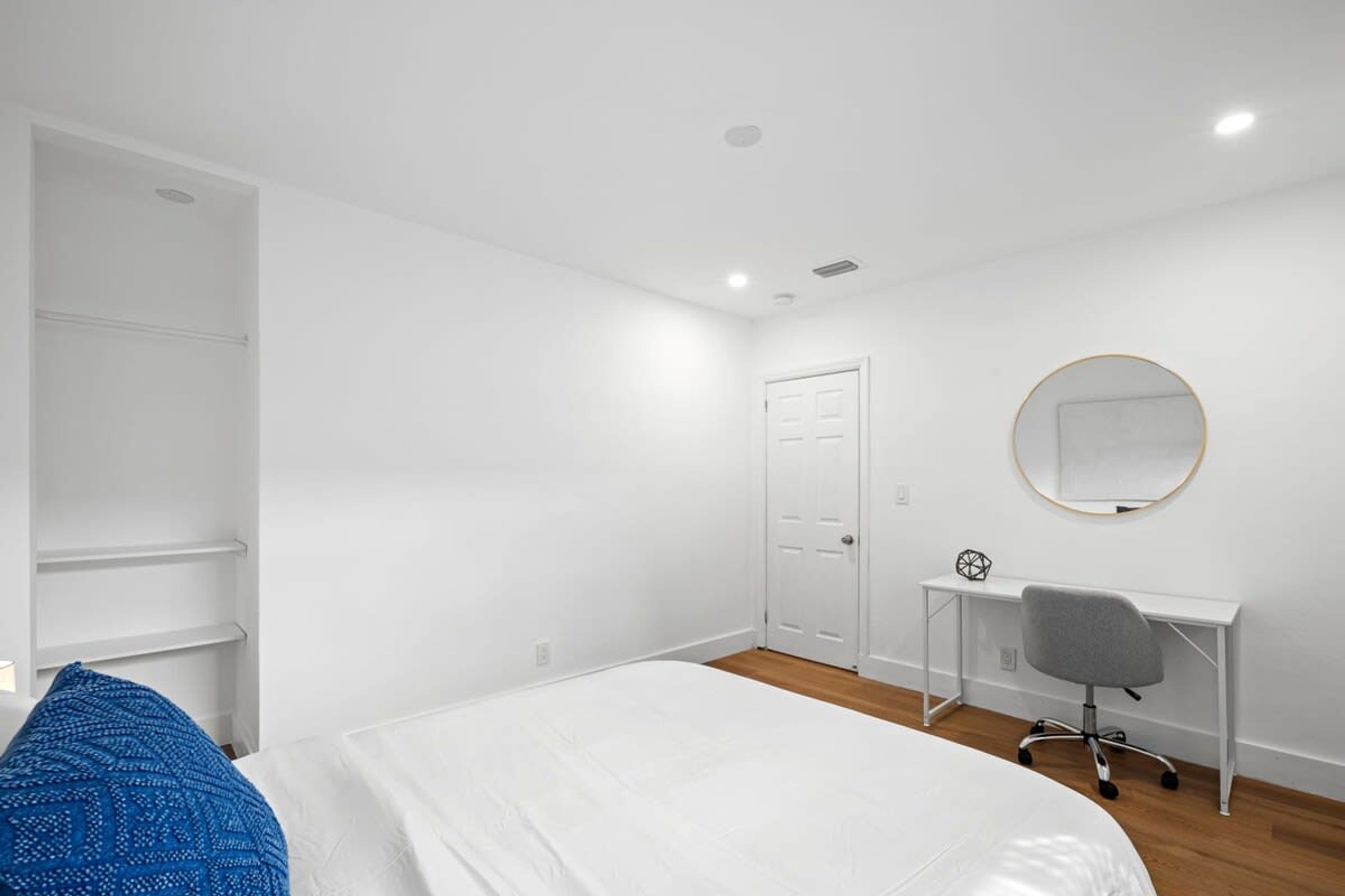 A bedroom with a bed, a desk, a chair, a wardrobe, and a mirror on the wall.