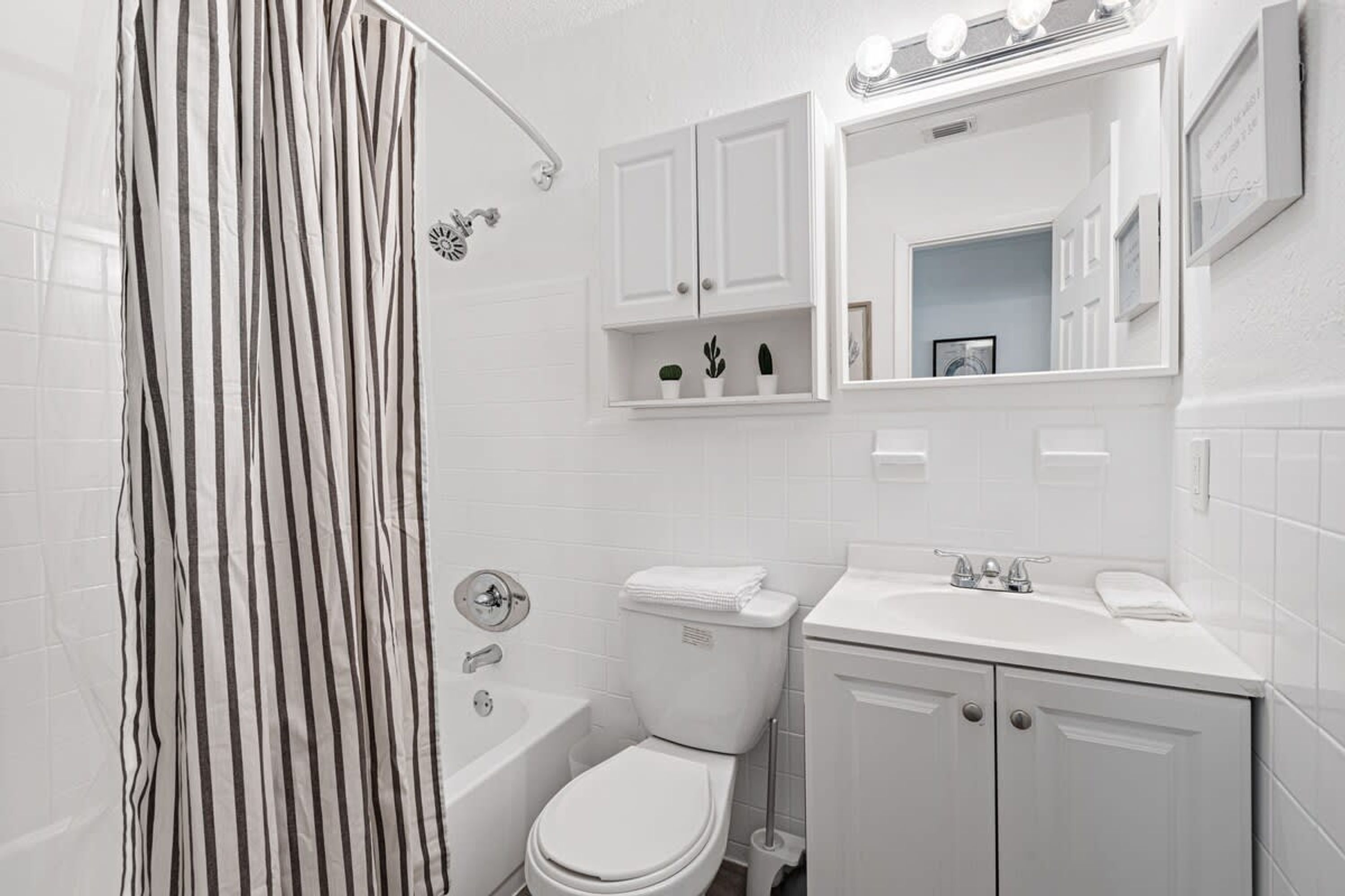 Un baño moderno con bañera, inodoro y lavamanos. Hay armarios blancos y un espejo sobre el lavamanos.