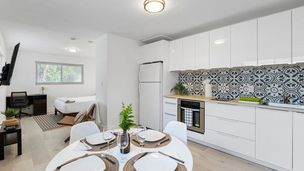 Una cocina moderna con armarios blancos, un salpicadero con estampado blanco y negro, y un comedor con una mesa redonda dispuesta para cuatro personas.