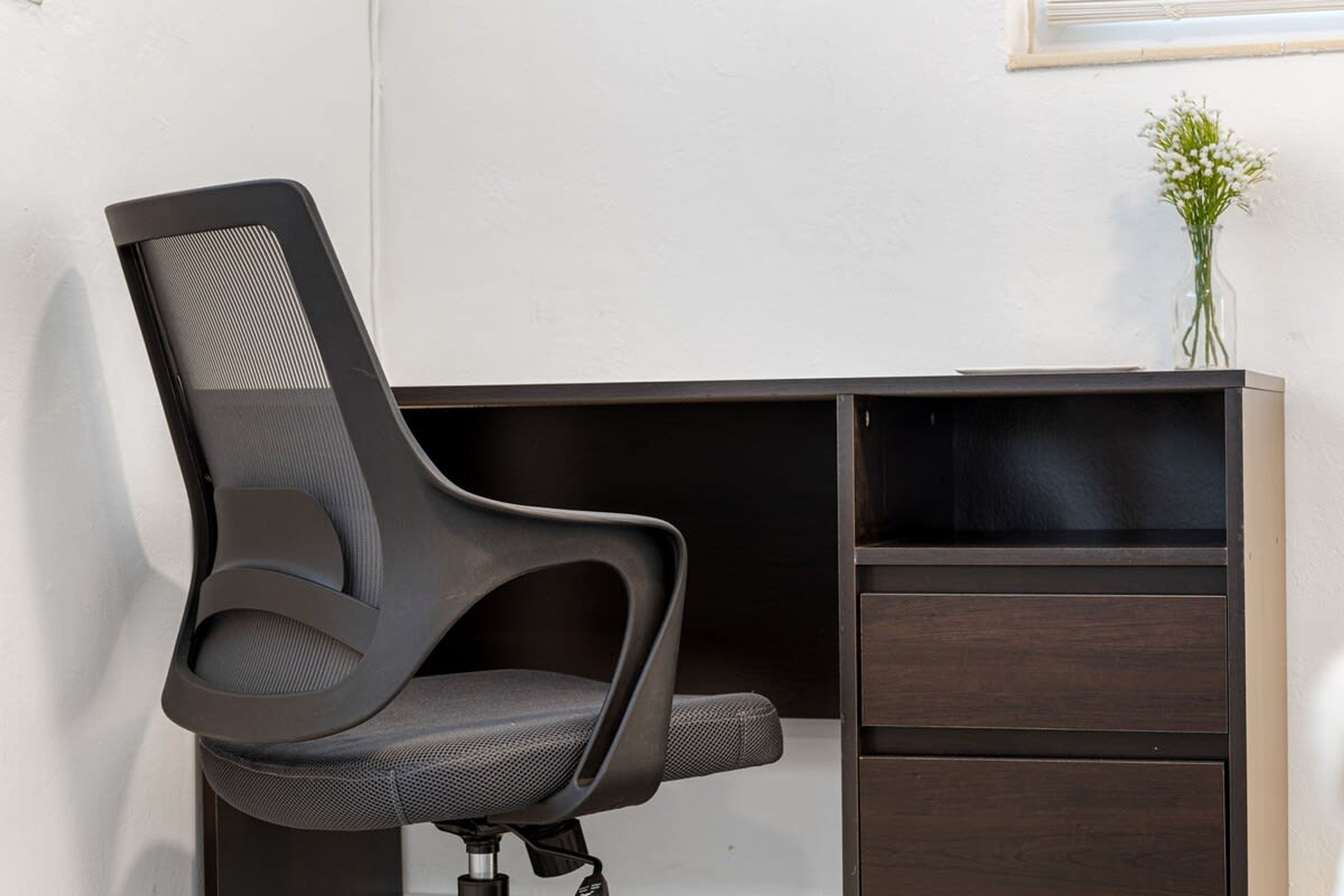 Un fauteuil de bureau moderne doté d’un dossier en tissu ajouré et d’un bureau marron foncé muni de plusieurs tiroirs.
