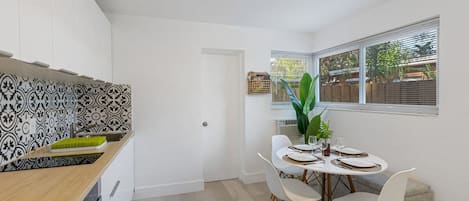 A modern kitchen with white cabinets, a patterned backsplash, and a dining area with a table set for four.