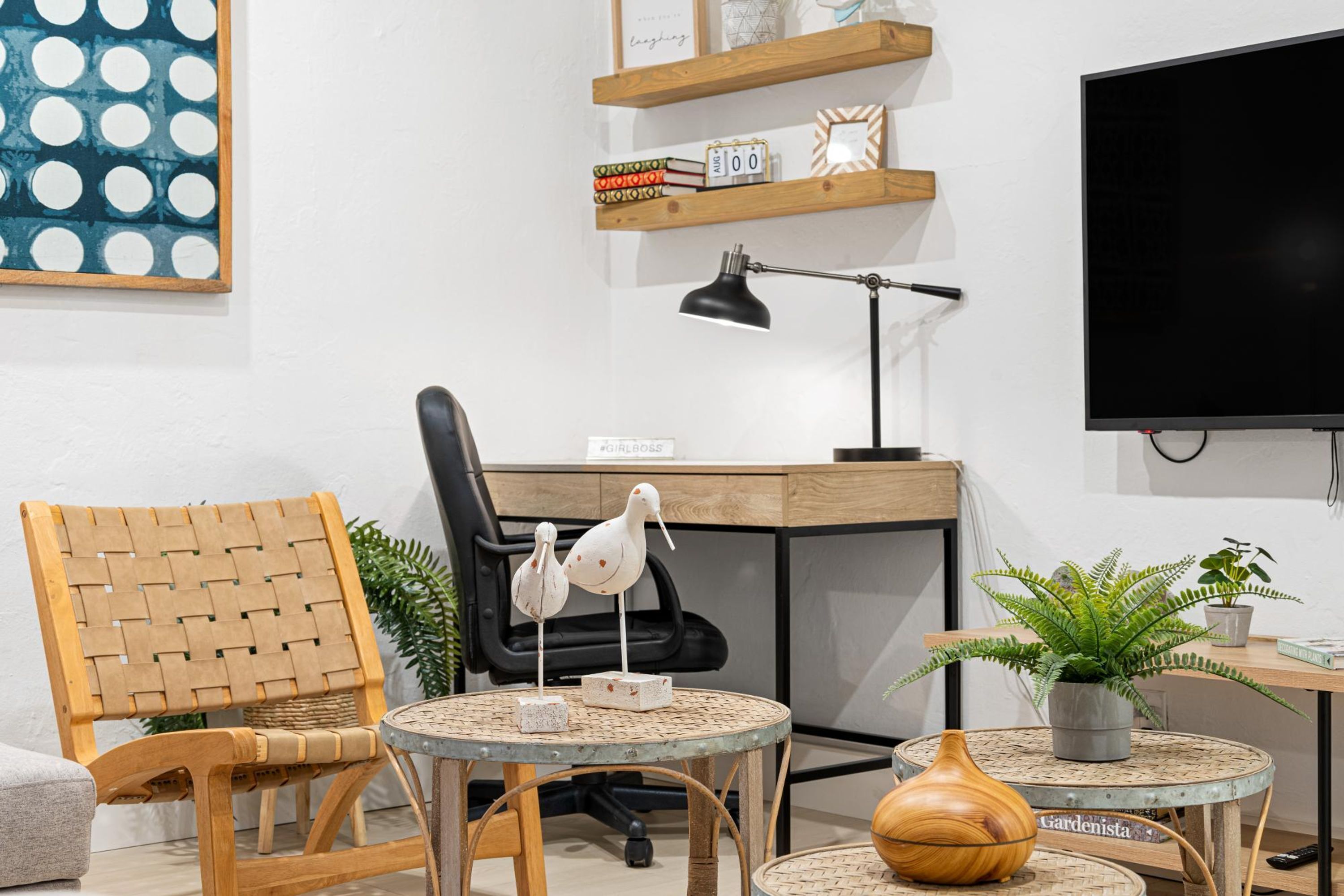Ein modernes Wohnzimmer mit einem Holzstuhl, einem runden Tisch mit einer Vase und einem Fernseher an der Wand.