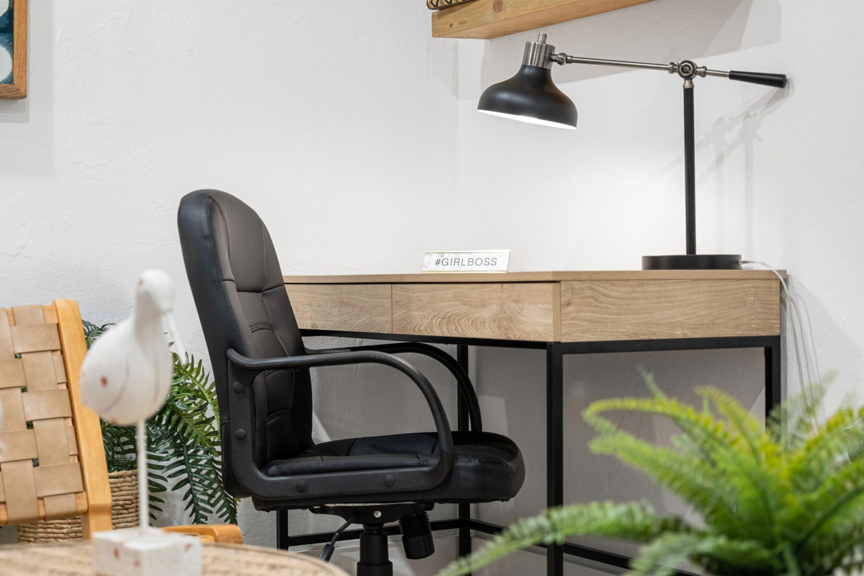 Una silla de oficina moderna, un escritorio con una lámpara y un cartel que dice '#GIRLBOSS'.