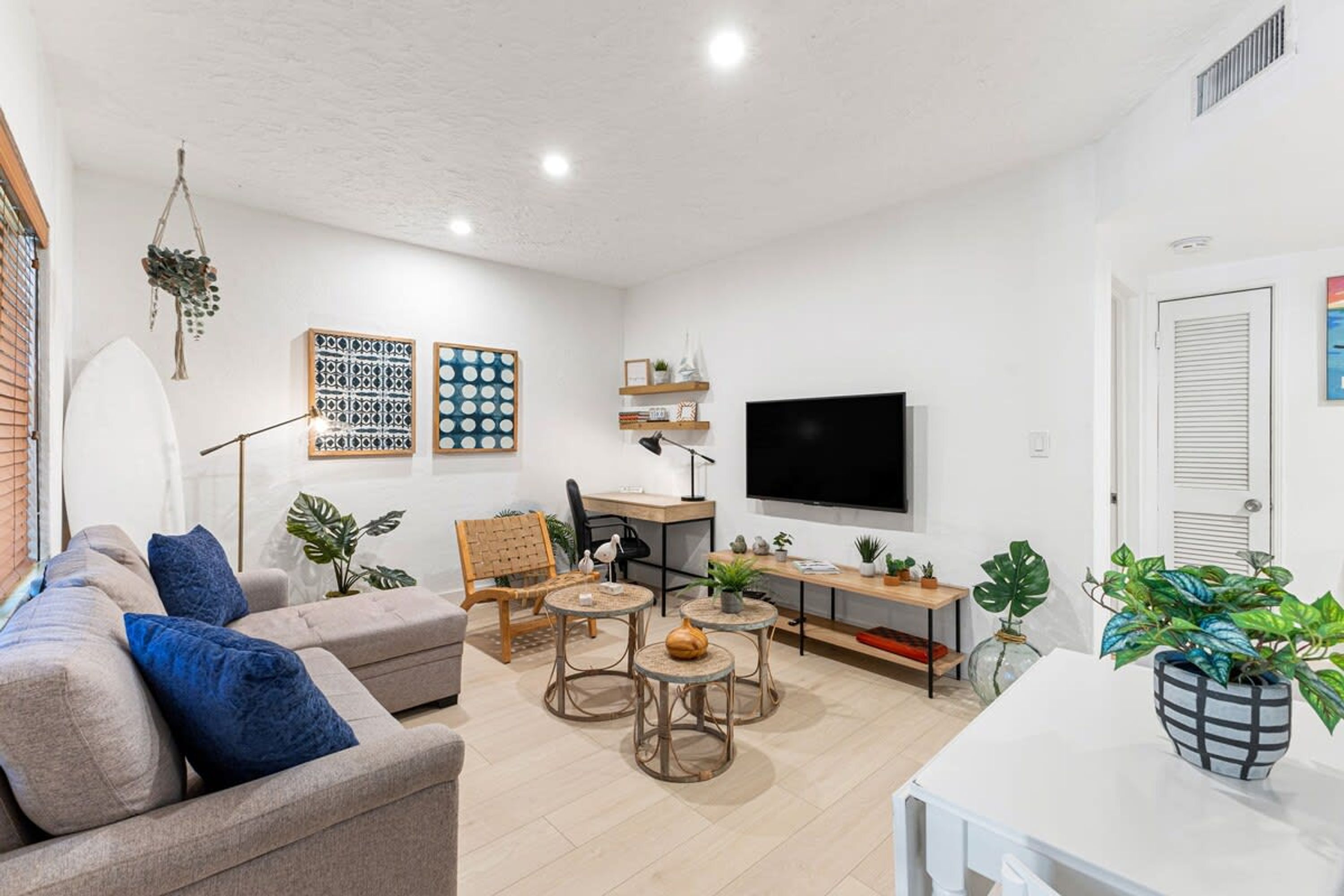 Una sala de estar moderna con un sofá, una mesa de centro y sillones. Hay un televisor montado en la pared y una estantería con objetos decorativos.