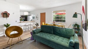 Un salon moderne avec un canapé vert, un fauteuil original de couleur moutarde et un coin repas avec des chaises jaunes.