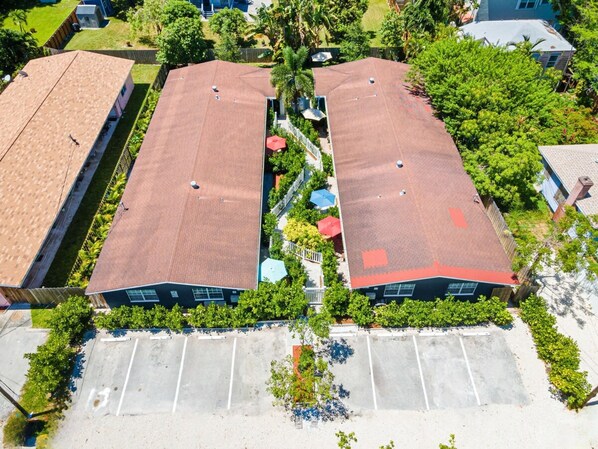 Un edificio de dos pisos con techo rojo, rodeado de vegetación y un estacionamiento.