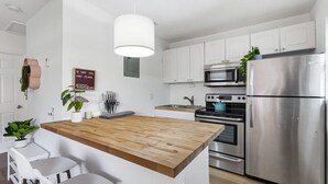 Une cuisine moderne avec des meubles blancs, un îlot central en bois, des appareils électroménagers en acier inoxydable et une plante suspendue.