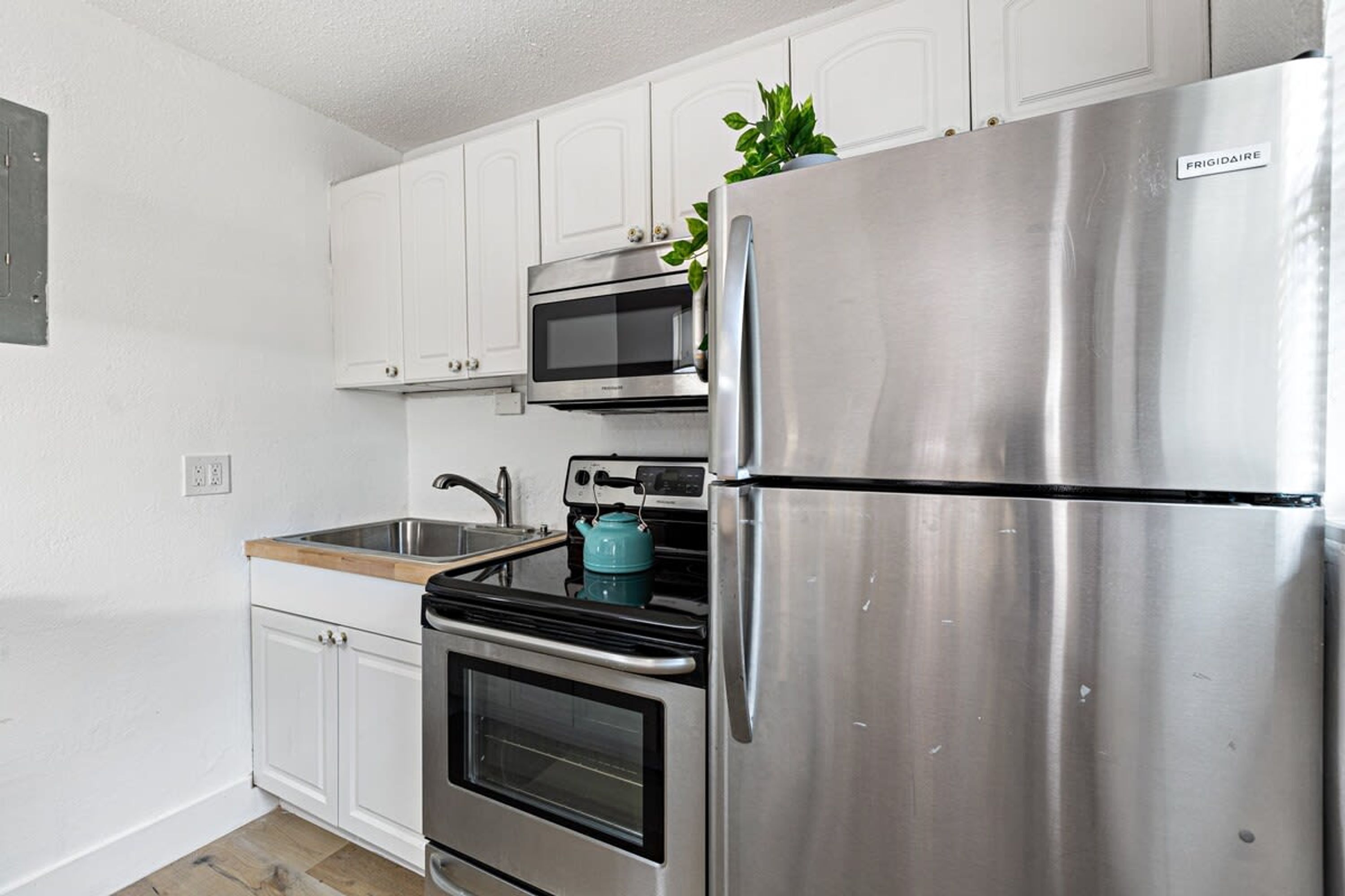 A modern kitchen with white cabinets, a stainless steel refrigerator, a built-in oven, a microwave, and a kettle.