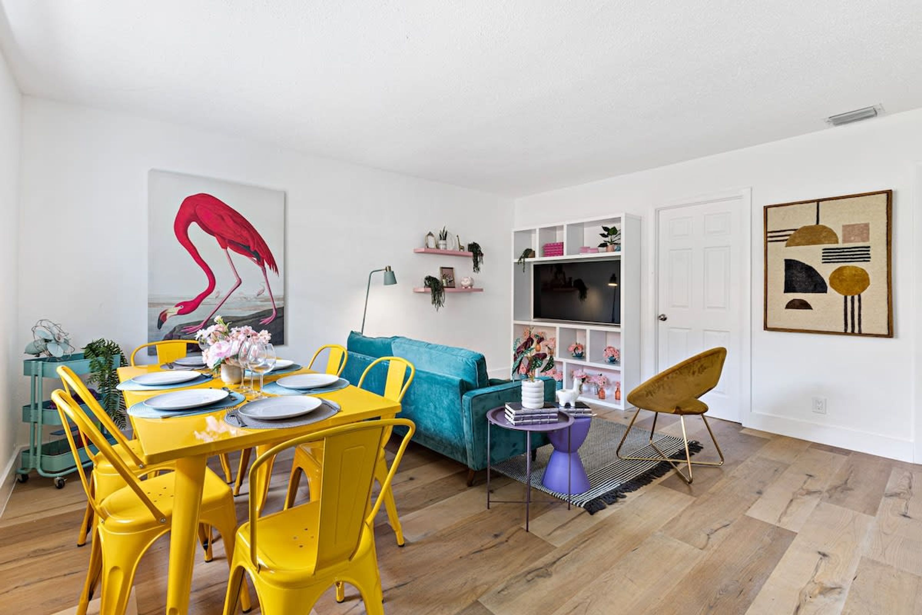 Une table de salle à manger jaune vif, assortie de chaises, un canapé turquoise et une table d’appoint violette.