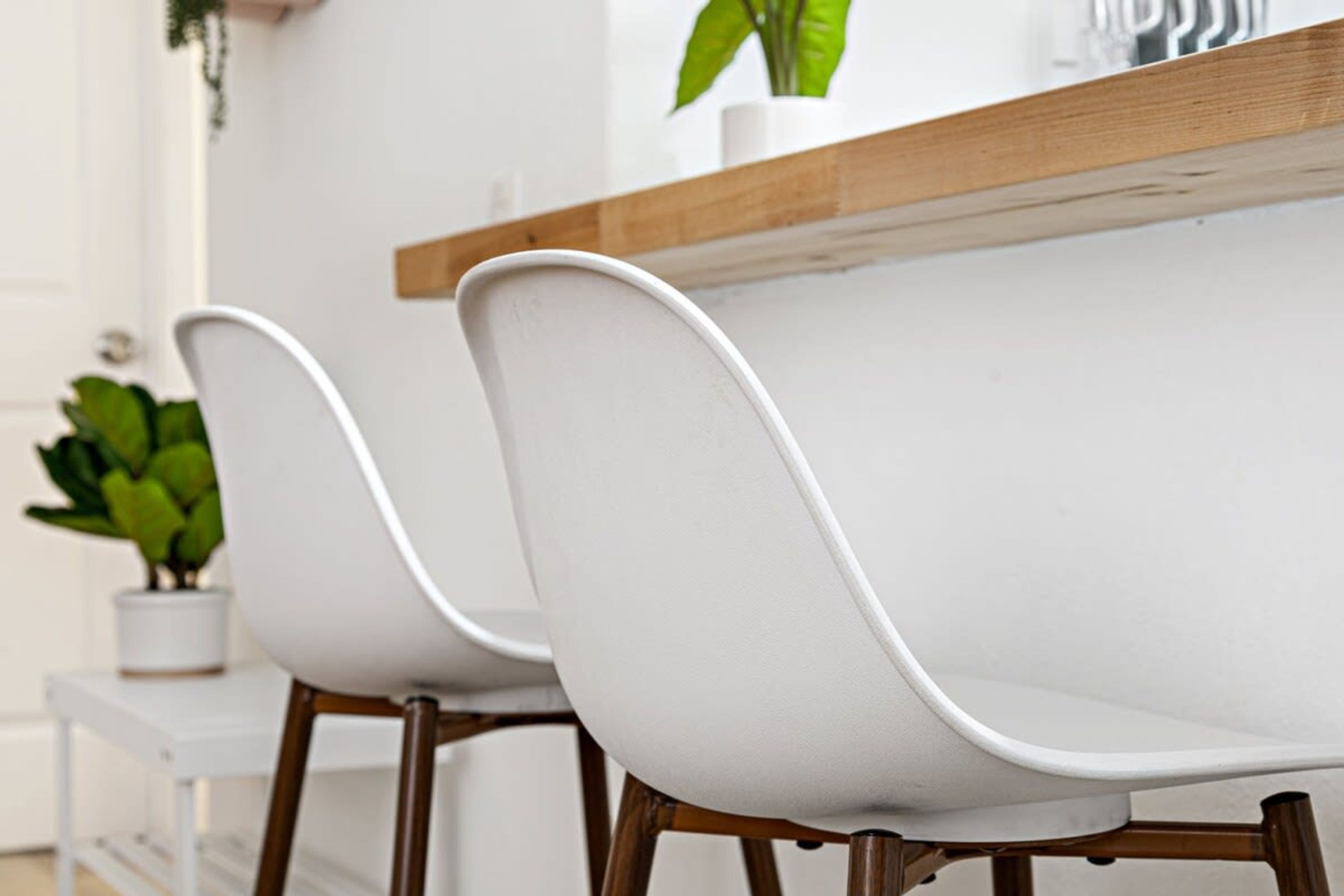 Deux chaises blanches avec des pieds en bois et une table blanche avec un plateau en bois.