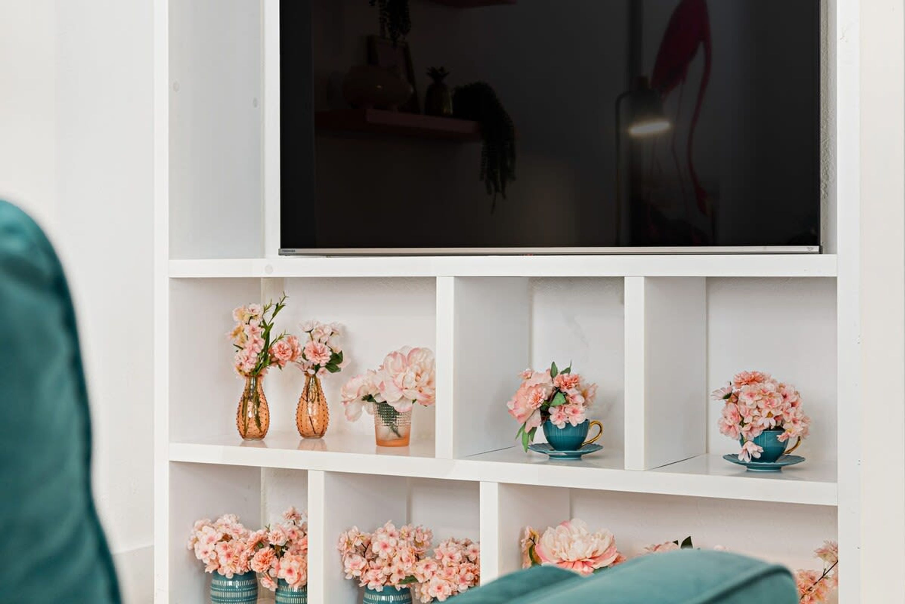 A white shelving unit with multiple vases of pink flowers.
