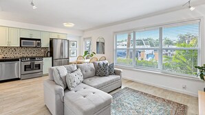 A modern kitchen with stainless steel appliances, a grey sectional sofa, and a large window with a view of the outside. - Las Olas Blvd Waterfront Apt (Fort Lauderdale)