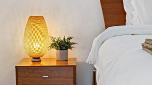 A bedroom with a wooden nightstand, a lamp, a potted plant, a bed with white bedding, and a window with blinds. - Las Olas Blvd Waterfront Apt (Fort Lauderdale)