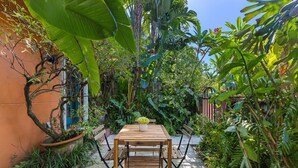 Eine Terrasse im Freien mit einem Holztisch und -stühlen, umgeben von üppiger Bepflanzung und einem Blumentopf.
