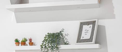 A white wall with multiple shelves displaying plants and books.
