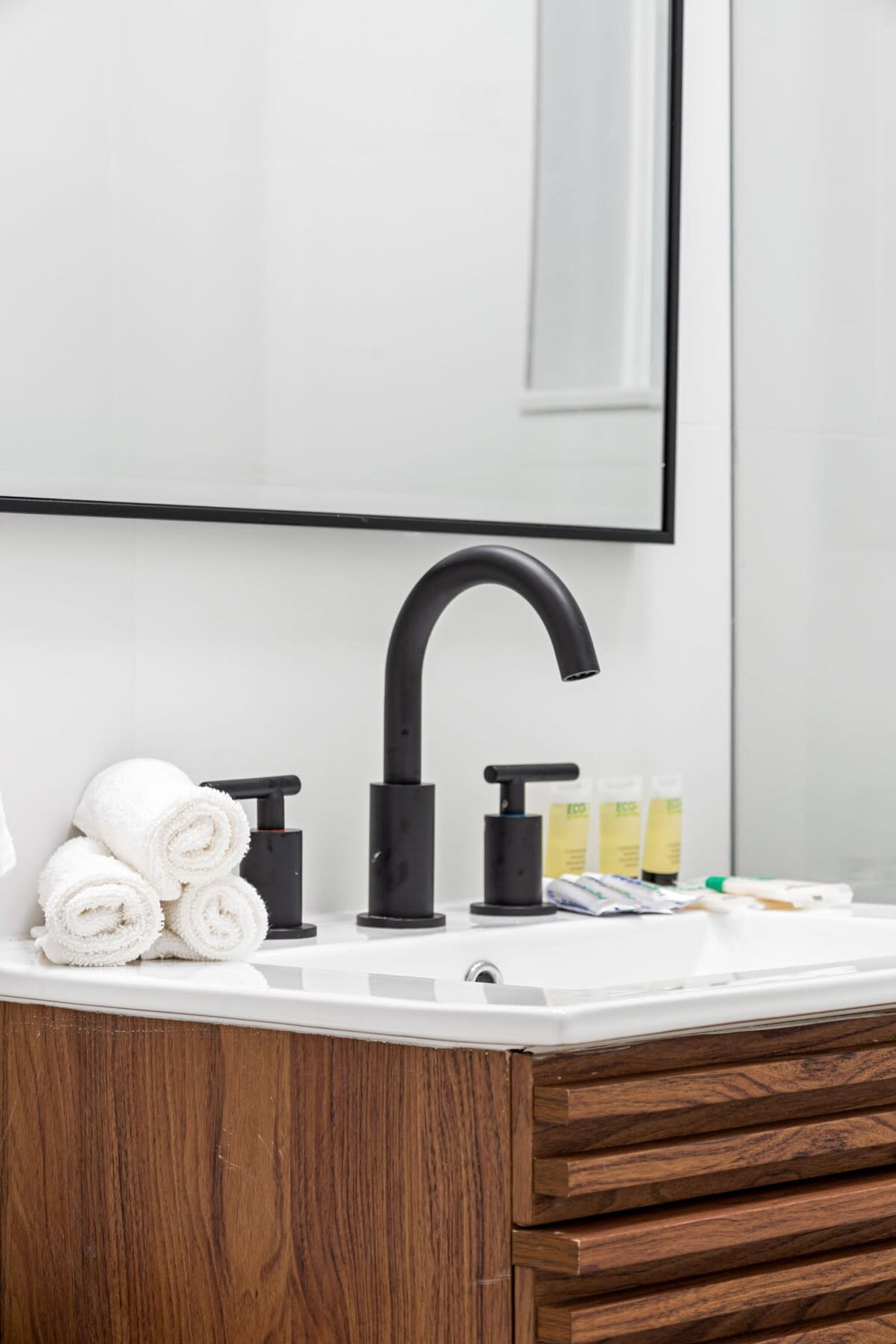 A bathroom with a white sink, black faucet, and wooden cabinet drawers.