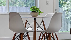 Un comedor con dos sillas blancas, una mesa redonda y una planta en maceta.