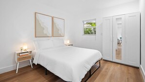 Un dormitorio con cama, mesitas de noche, armario y cuadros en la pared.