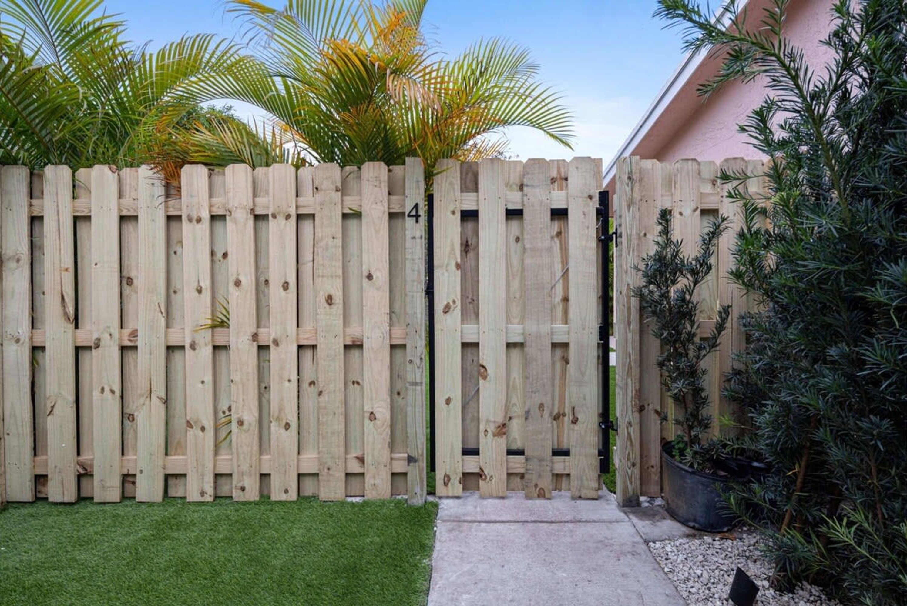 A wooden fence with a gate, a concrete pathway, and a small patch of artificial grass.