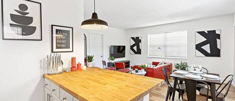 A modern kitchen with a wooden island, white cabinets, and a dining area with a red chair and a table set for two.
