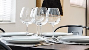 A dining table set with white plates and clear wine glasses, with a black chair visible. - Lovely 2 BR Condo With Free Parking on Premises (Fort Lauderdale)
