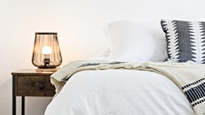 A neatly made bed with a white comforter and a patterned throw blanket. A bedside table with a lamp is visible to the left. - Lovely 2 BR Condo With Free Parking on Premises (Fort Lauderdale)