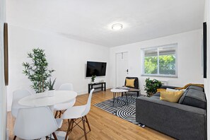 Ein modernes Wohnzimmer mit Essbereich, einem Flachbildfernseher, einer Couch und einer Topfpflanze.