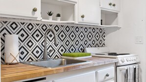 A kitchen with white cabinets, a black and white patterned backsplash, a stainless steel sink, a wooden countertop, a white stove, and a dish rack with green utensils. - Lake Ridge Villa - Free Parking (Fort Lauderdale)