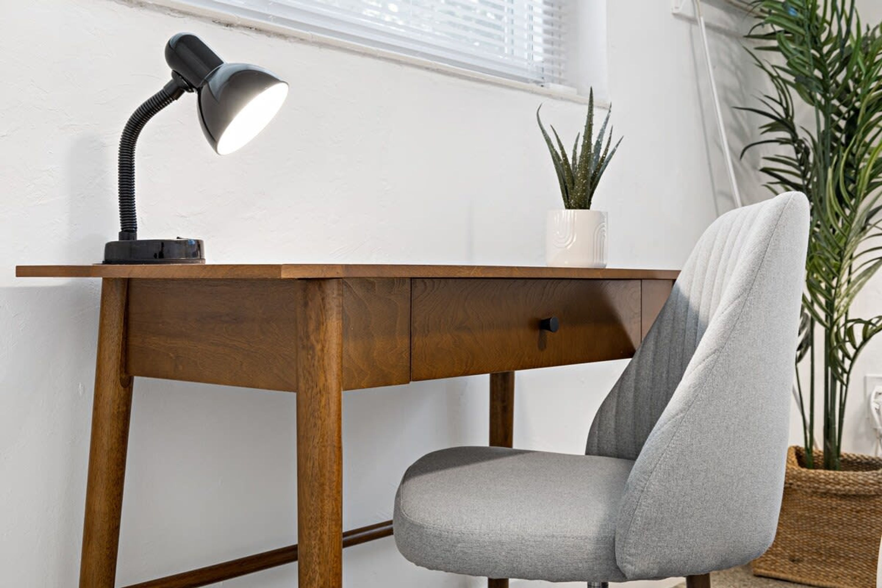 Ein Holztisch mit einer schwarzen Schreibtischlampe, ein grauer Stuhl und ein Blumentopf.