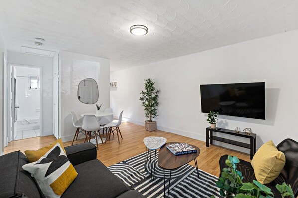 Ein modernes Wohnzimmer mit einer Couch, einem Couchtisch, einem Fernseher und einem Essbereich mit Stühlen und einem Tisch.