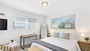 A modern hotel room with a large bed, a desk, a chair, and a small table. - Lovely Studio With Great Location Free Parking (Fort Lauderdale)