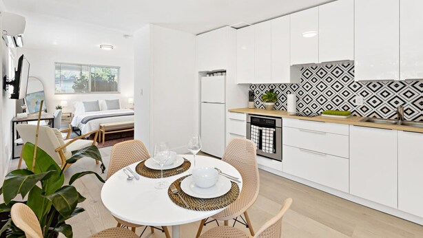 A modern kitchen with white cabinets, a patterned backsplash, and a dining area with a white table and wicker chairs. - Lovely Studio With Great Location Free Parking (Fort Lauderdale)
