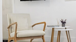 A modern room with a wooden chair, a small round table with a book and a plant, and a flat-screen TV mounted on the wall. - Lovely Studio With Great Location Free Parking (Fort Lauderdale)