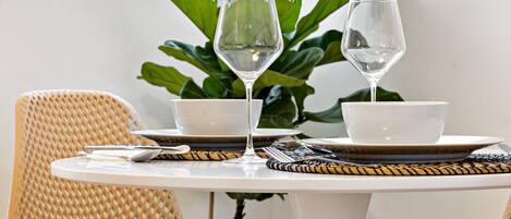 Una mesa redonda para comer con dos cuencos blancos y dos copas de vino, adornada con un mantel tejido.