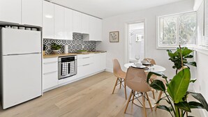 A modern kitchen with white cabinets, a built-in oven, and a dining area with a round table and wicker chairs. - Lovely Studio With Great Location Free Parking (Fort Lauderdale)