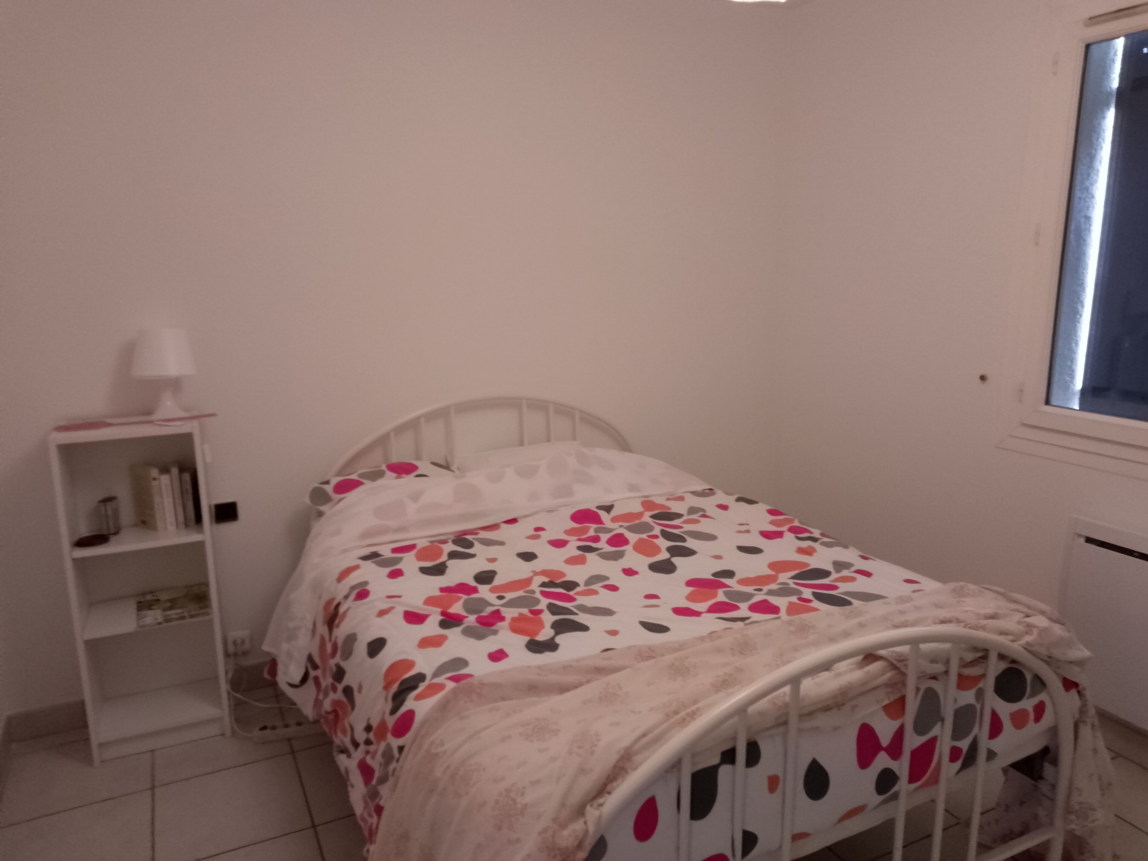 Une chambre à coucher avec un lit, une table de chevet, une lampe et une fenêtre.