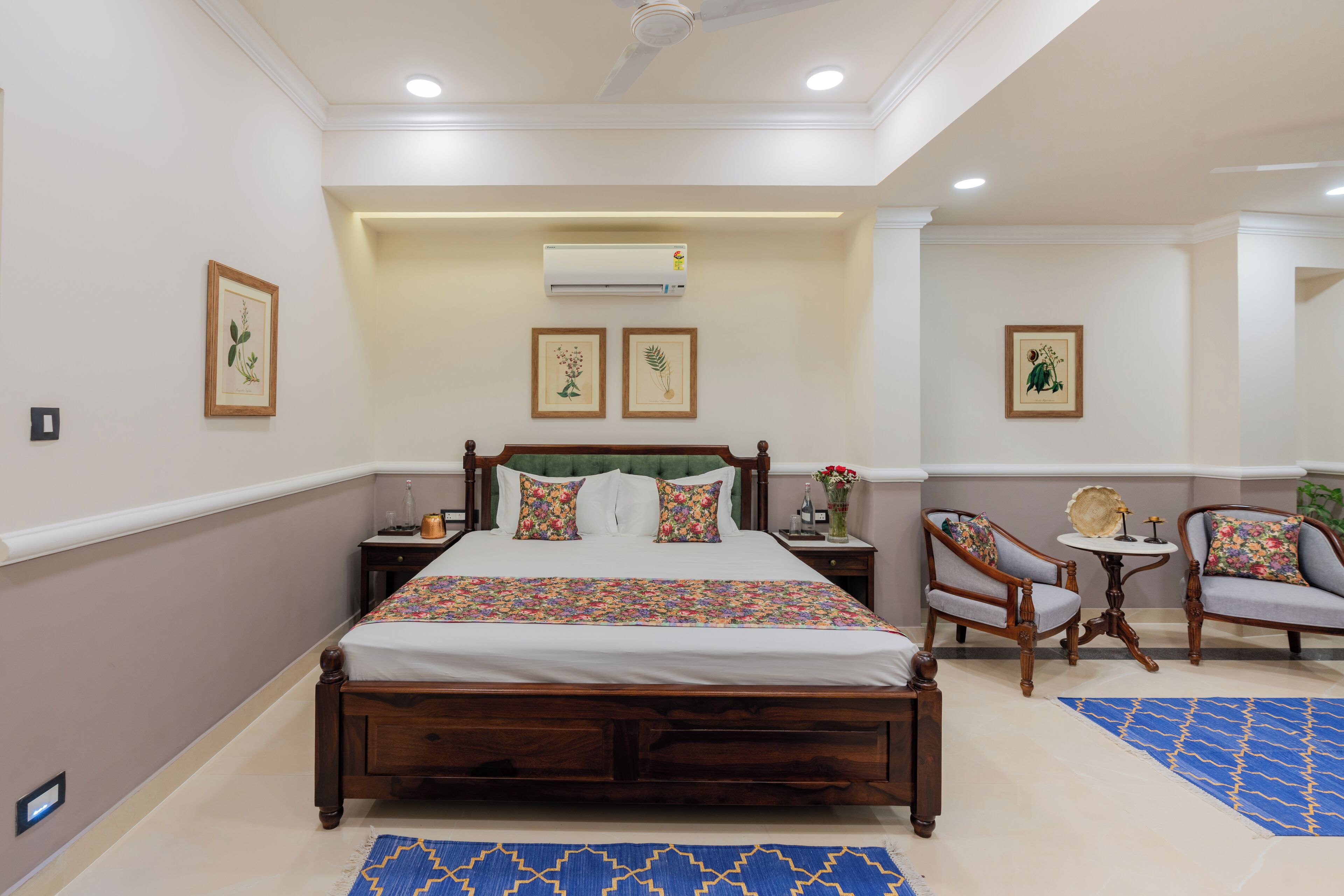 A bedroom with a wooden bed, two chairs, a small round table, and framed pictures on the walls.