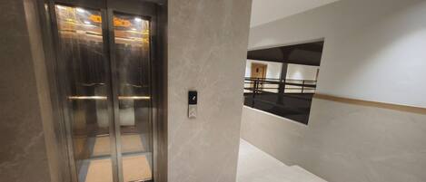 An elevator with a digital display showing the number 2, a glass door, and a hallway with a marble floor and a black railing.