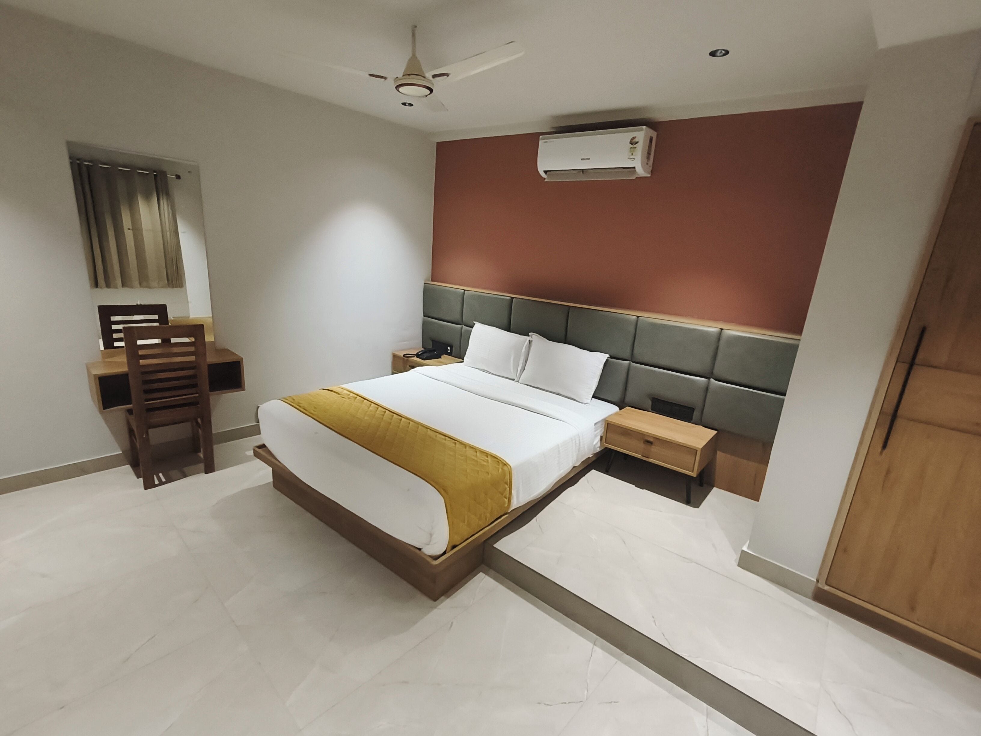 A bedroom with a bed, bedside tables, a desk, a chair, a ceiling fan, and an air conditioning unit.