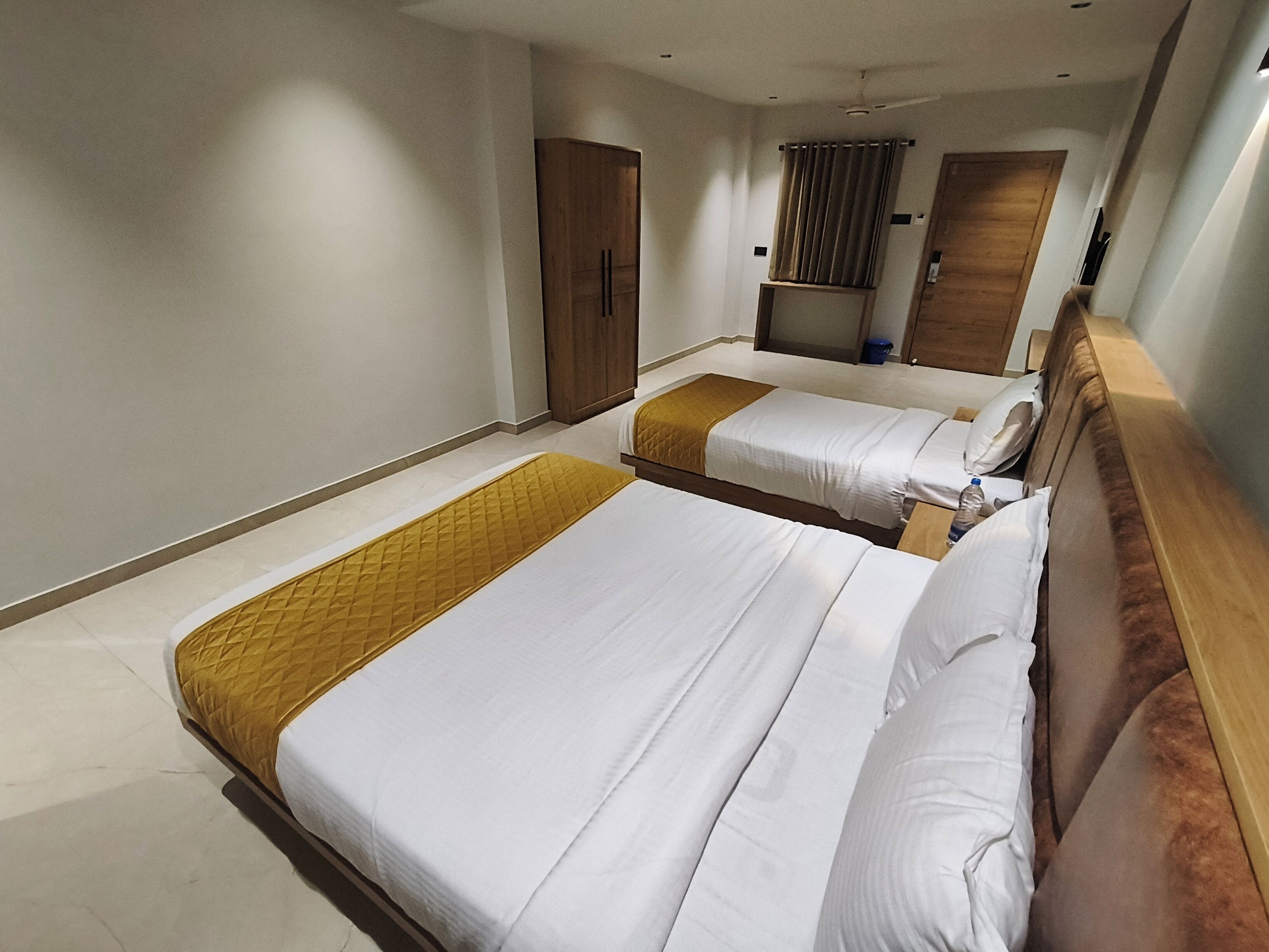 A hotel room with two beds, a wardrobe, a mirror, and a ceiling fan.