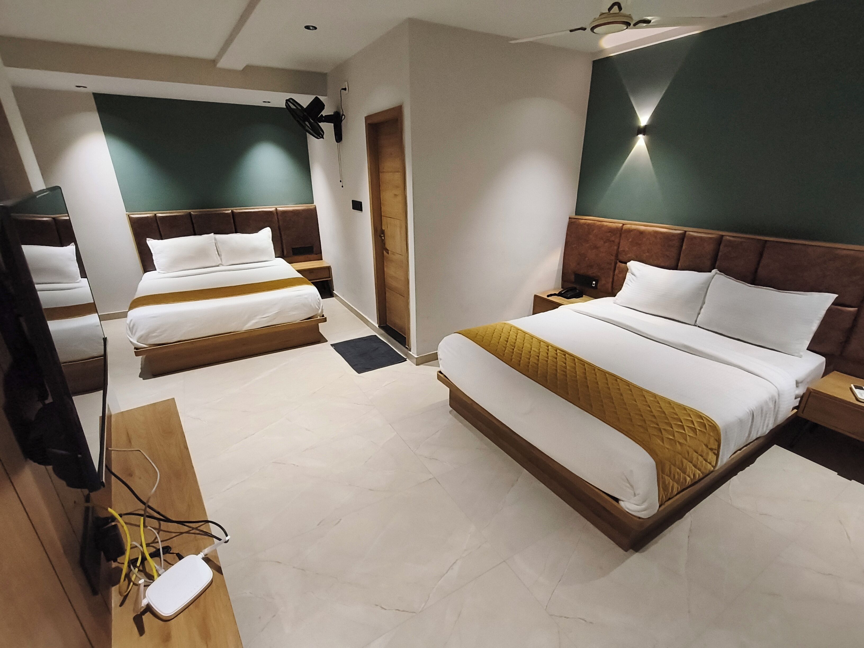 A hotel room with two beds, a desk, a chair, a TV, and a ceiling fan.