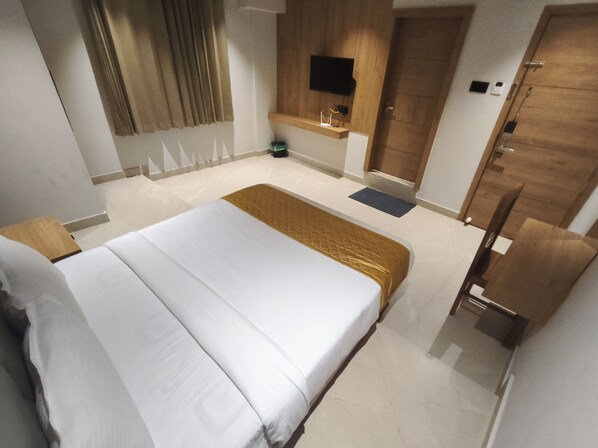 A hotel room with a bed, a desk, a chair, a TV mounted on the wall, and a wardrobe. - Hotel Beverly Plaza Kozhikode (Kozhikode)