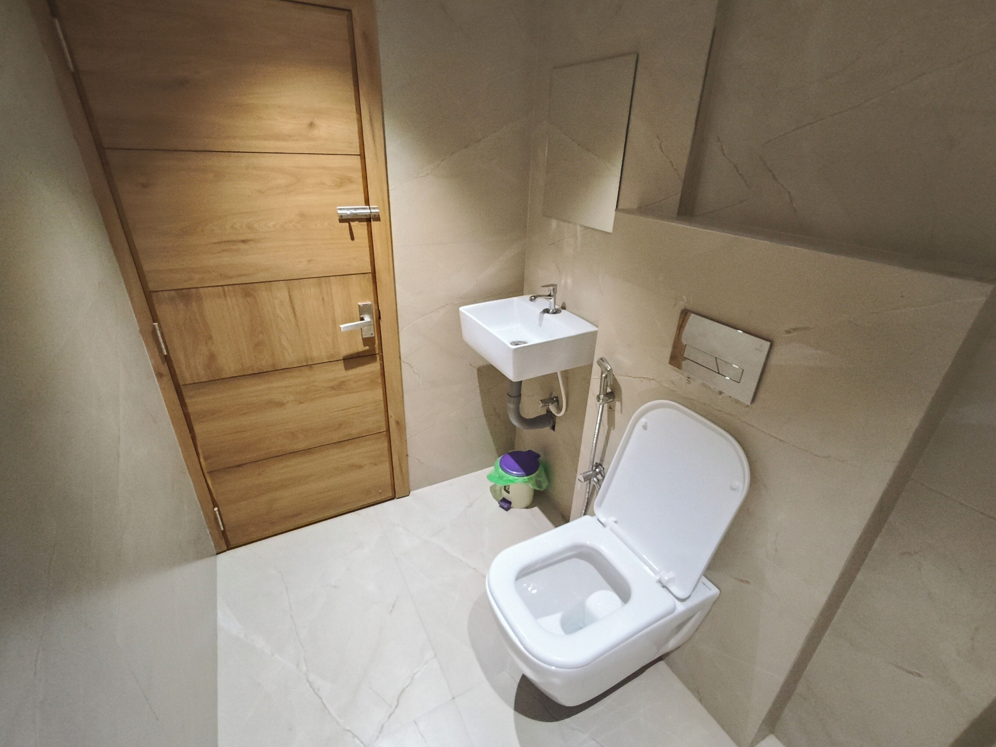 A small bathroom with a wooden door, a white sink, a toilet, and a mirror.