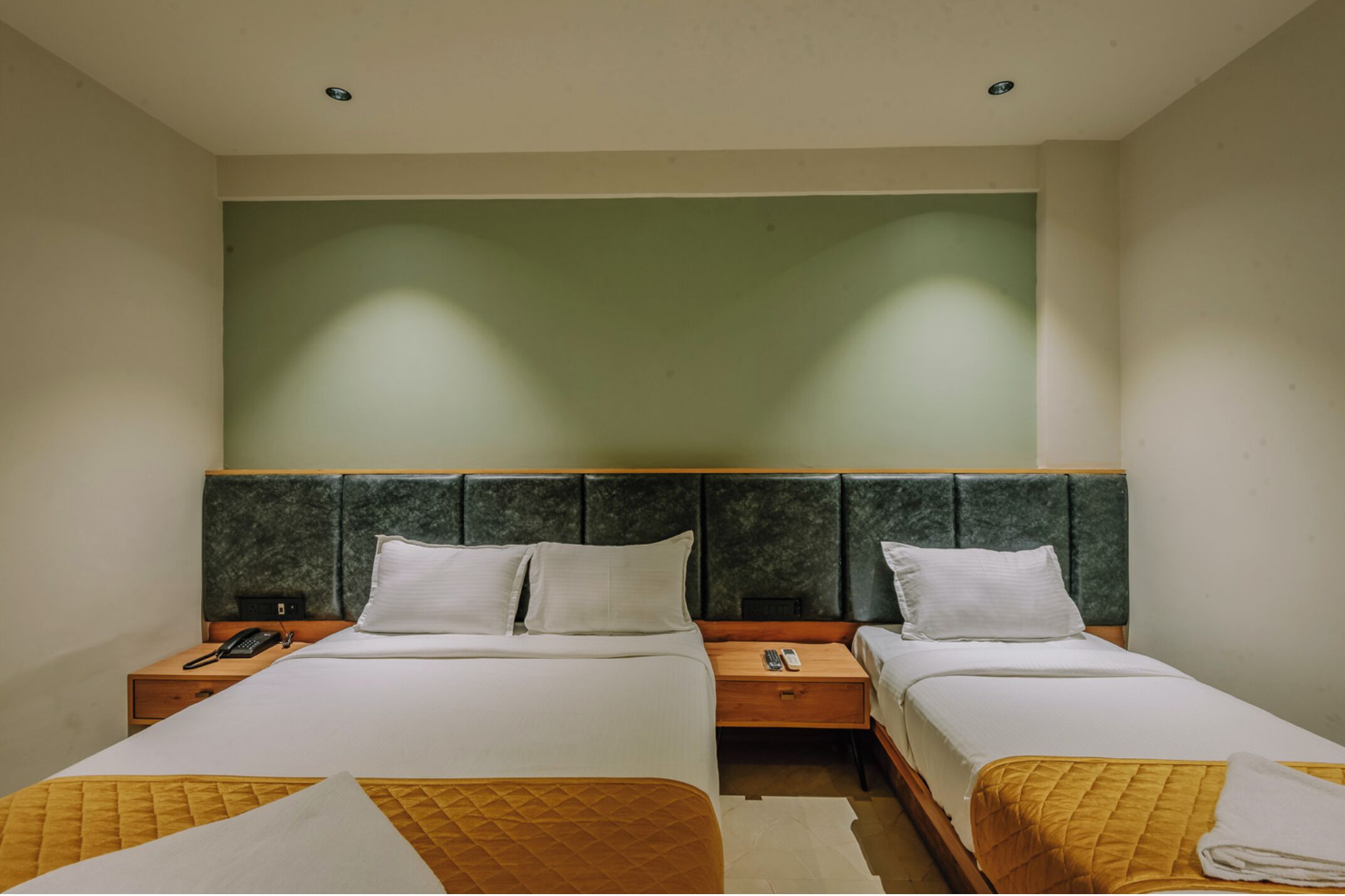 A hotel room with two beds, a green headboard, and a small bedside table with a phone.