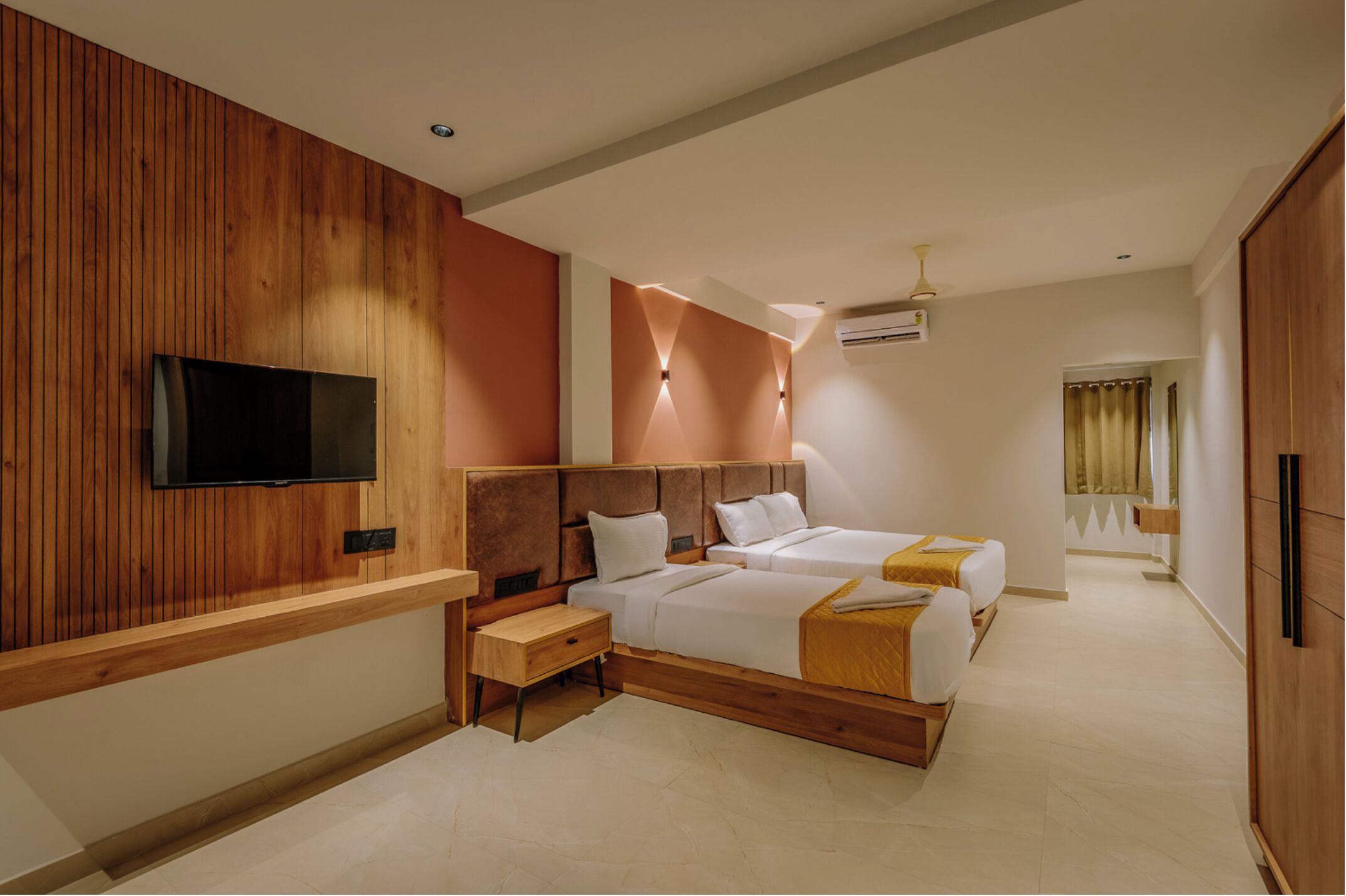 Camera d'hotel moderna con parete in legno, televisione a schermo piatto montata sopra una panca di legno e un letto con lenzuola bianche e coperta gialla.
