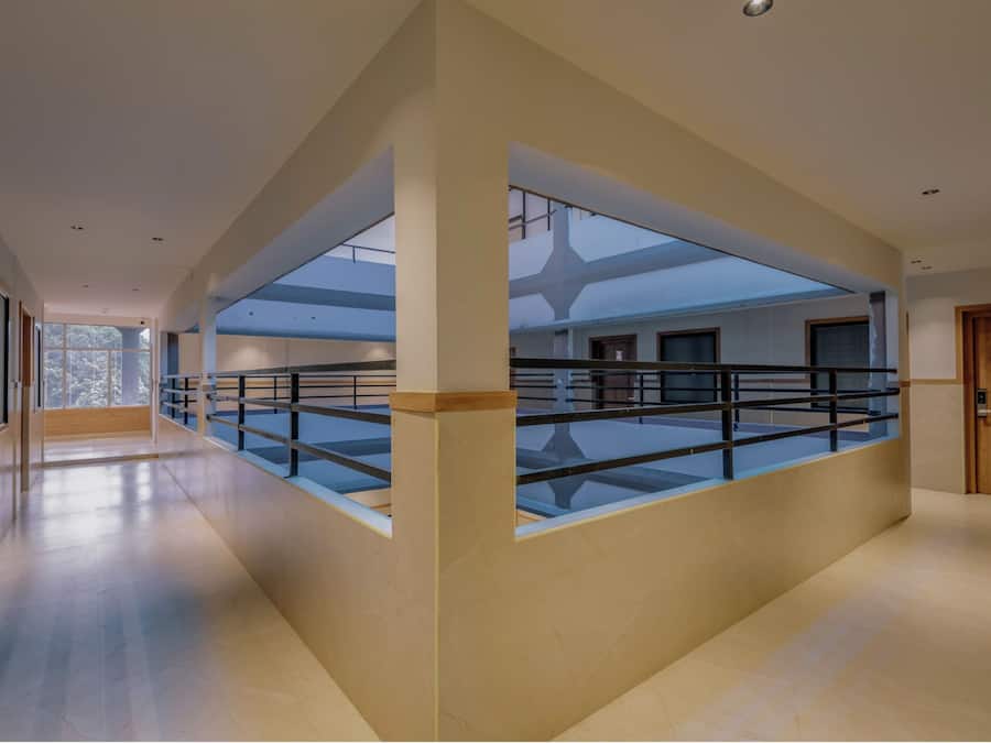 A spacious corridor with a glass railing, wooden doors, and a high ceiling.